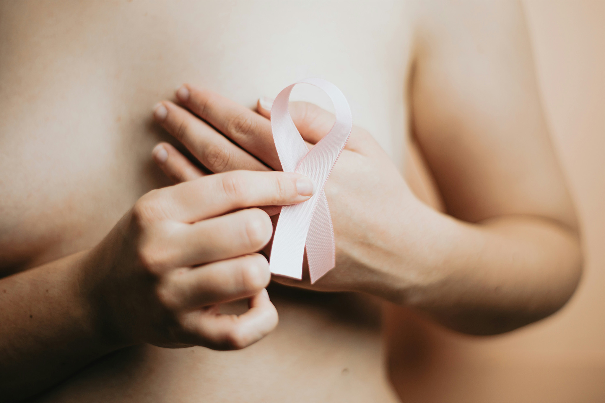 Woman holding a pink breast cancer ribbon over her chest, symbolizing awareness, hope, and the fight for a cure - what are the cures for breast cancer 